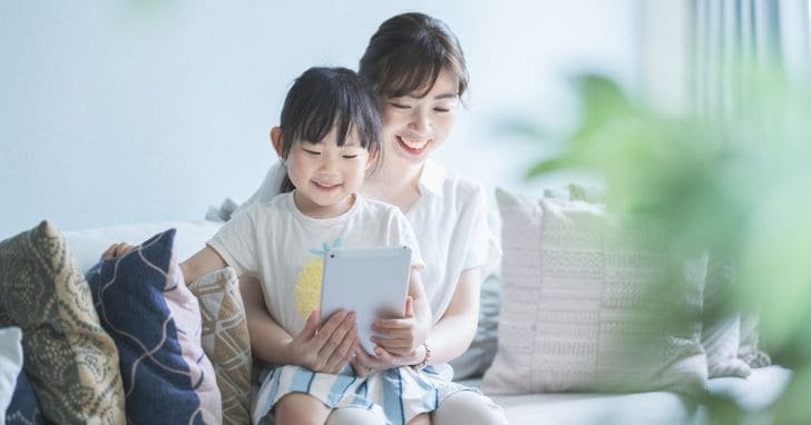 女性とその膝の上に乗る女の子が2人でタブレットを見て楽しんでいる様子
