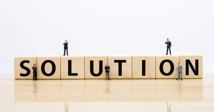 SOLUTIONと1文字ずつ書かれた積み木とその周囲で考えるビジネスマンの人形