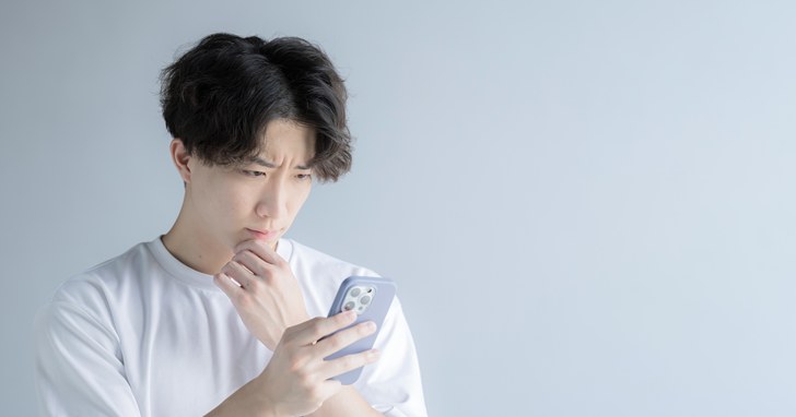 スマートフォンを見ながら悩んでいる男性のイメージ