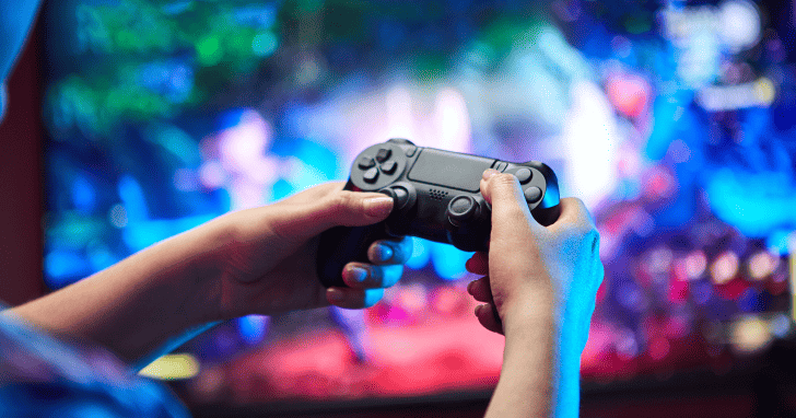 ゲームコントローラーを両手で持ち、モニターに映る画面を見ながらゲームをしているイメージ